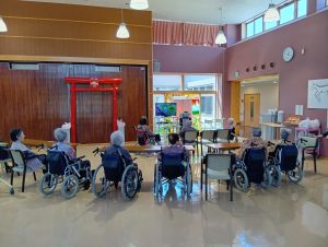 介護施設のレク・運動プログラム。車椅子利用者が円形に集まり、スタッフが指導する風景
