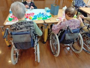 車椅子利用者が作業療法やアート活動に参加している風景。木製テーブルで創作活動中。